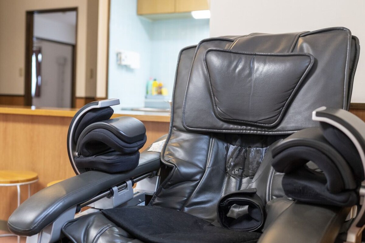 A massage chair with a headrest and footrest, a wooden counter with stools, and a kitchen area in the background.