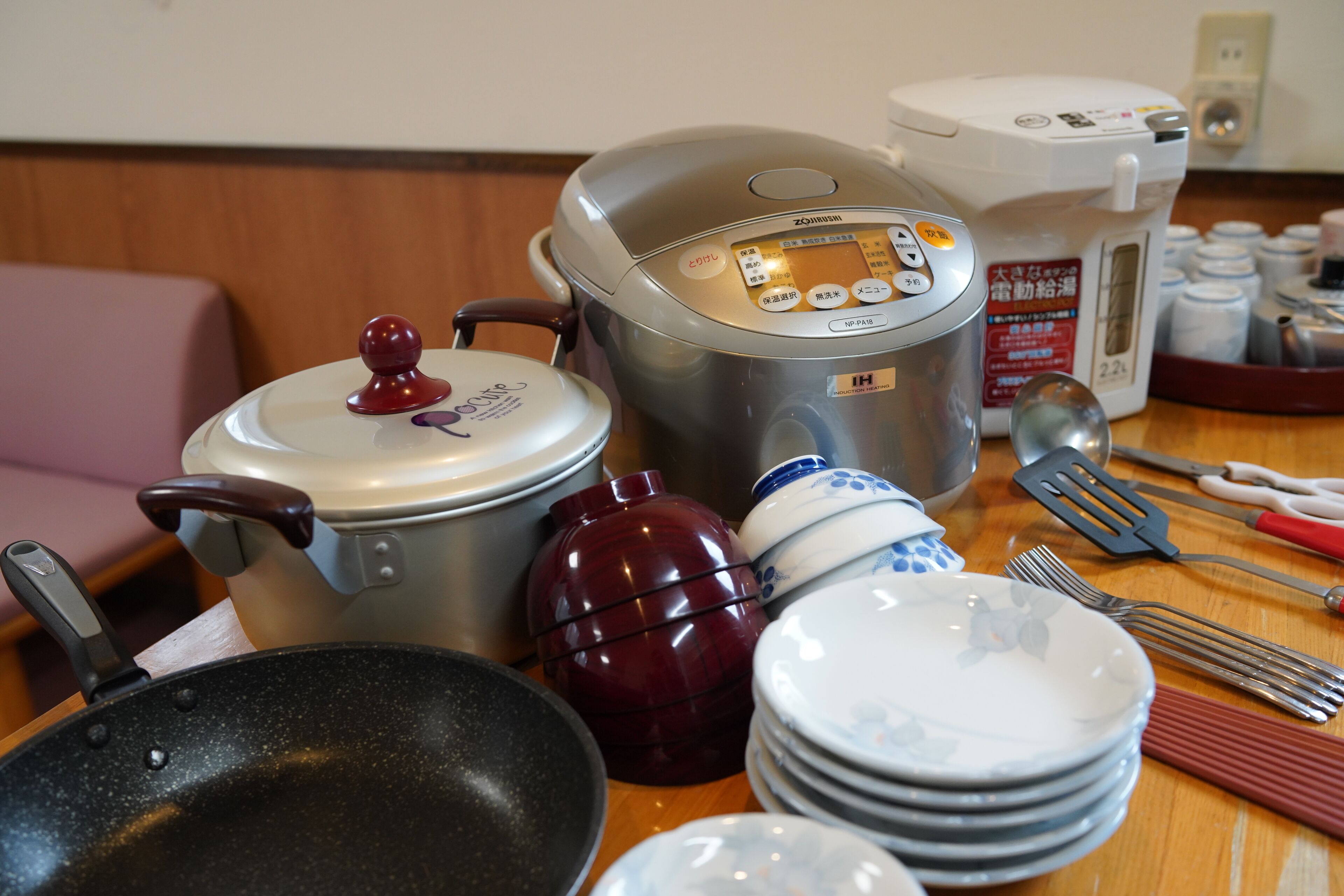 A kitchen with a rice cooker, a pot, a pan, and various utensils.