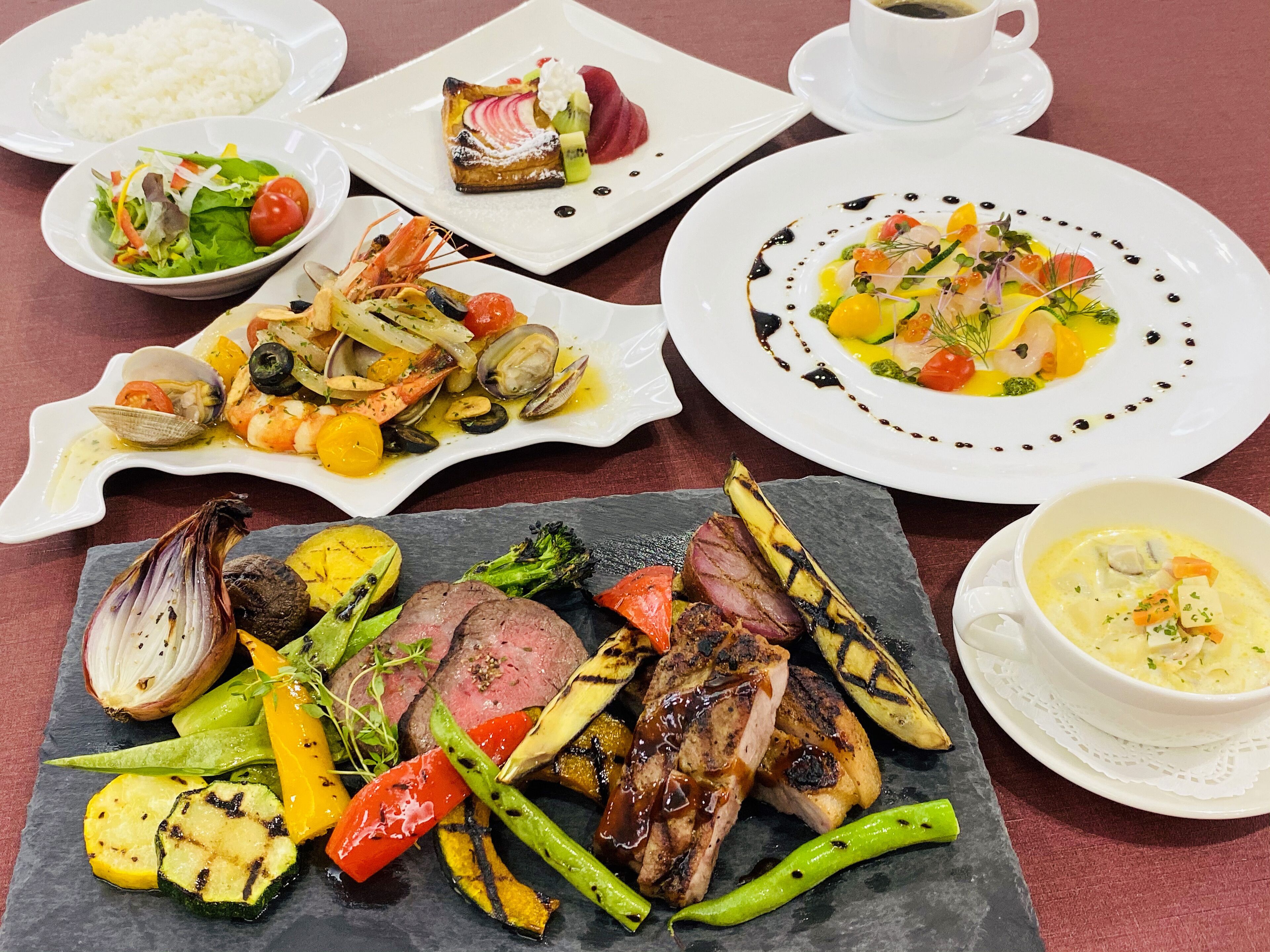 Diversos pratos, incluindo legumes grelhados, frutos do mar e carnes, servidos em vários pratos e uma lousa.