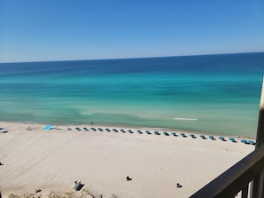 Uma praia com águas cristalinas turquesa, areal arenoso e guarda-sóis azuis.
