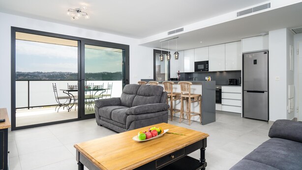 A modern apartment with a balcony, grey sofa, wooden coffee table, and a kitchen with white cabinets and stainless steel appliances. - Arenal Dream IV - Javea, Costa Blanca (Javea)