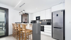A modern kitchen with white cabinets, a stainless steel refrigerator, and wooden bar stools. - Arenal Dream IV - Javea, Costa Blanca (Javea)