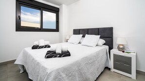 A neatly made bed with white linens and a patterned bedspread, a bedside table with a lamp, and a window with a view of the sky. - Arenal Dream IV - Javea, Costa Blanca (Javea)
