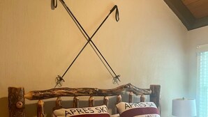 Ein Schlafzimmer mit einem Bett, zwei Kissen mit dem Aufdruck 'APRES SKI', einem Holz-Kopfteil und einem Fenster mit Jalousien.