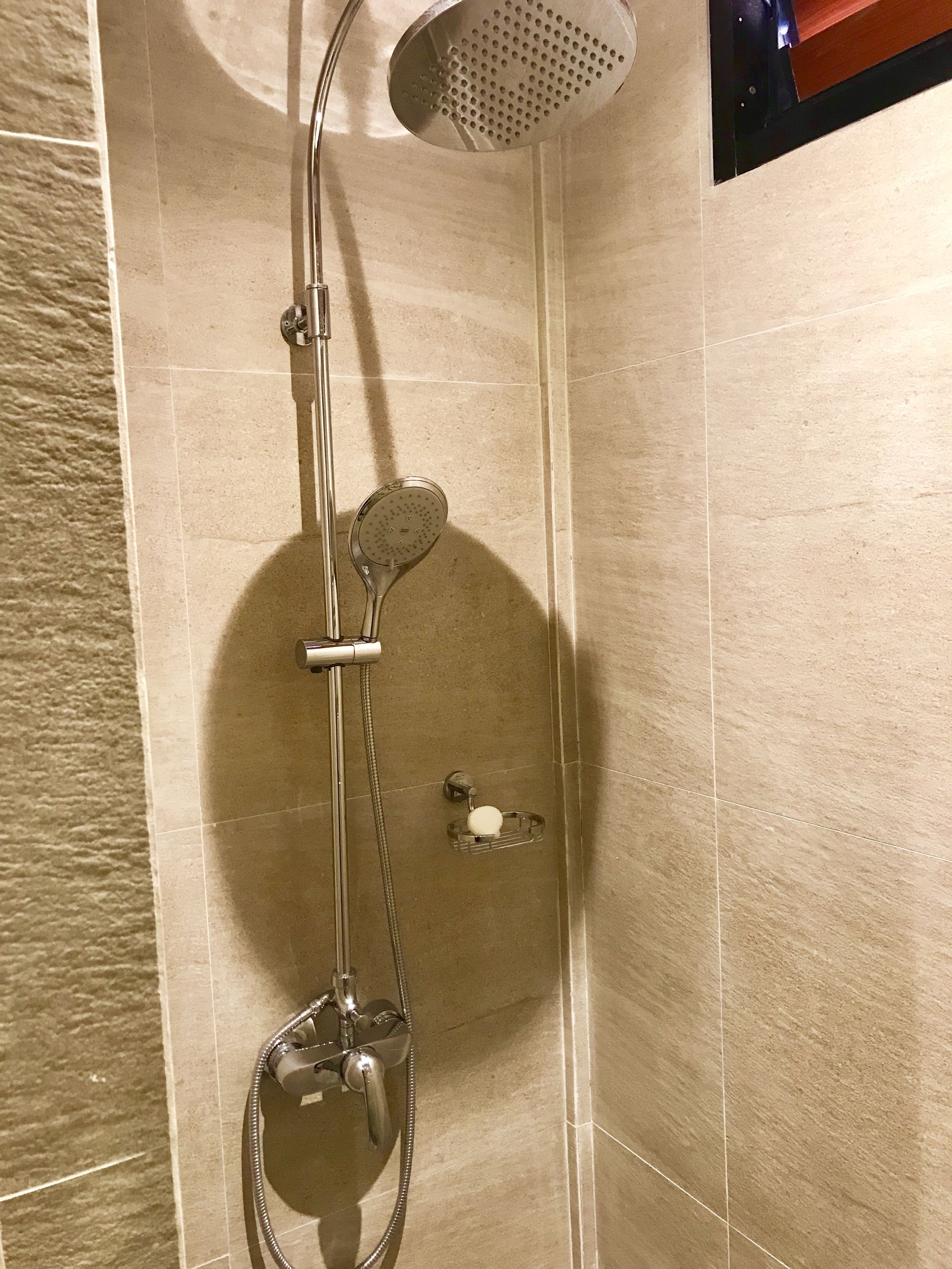 A shower with a handheld showerhead, a wall-mounted faucet, and a soap dish.