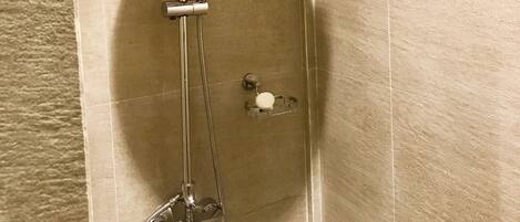 A shower with a handheld showerhead, a wall-mounted faucet, and a soap dish.