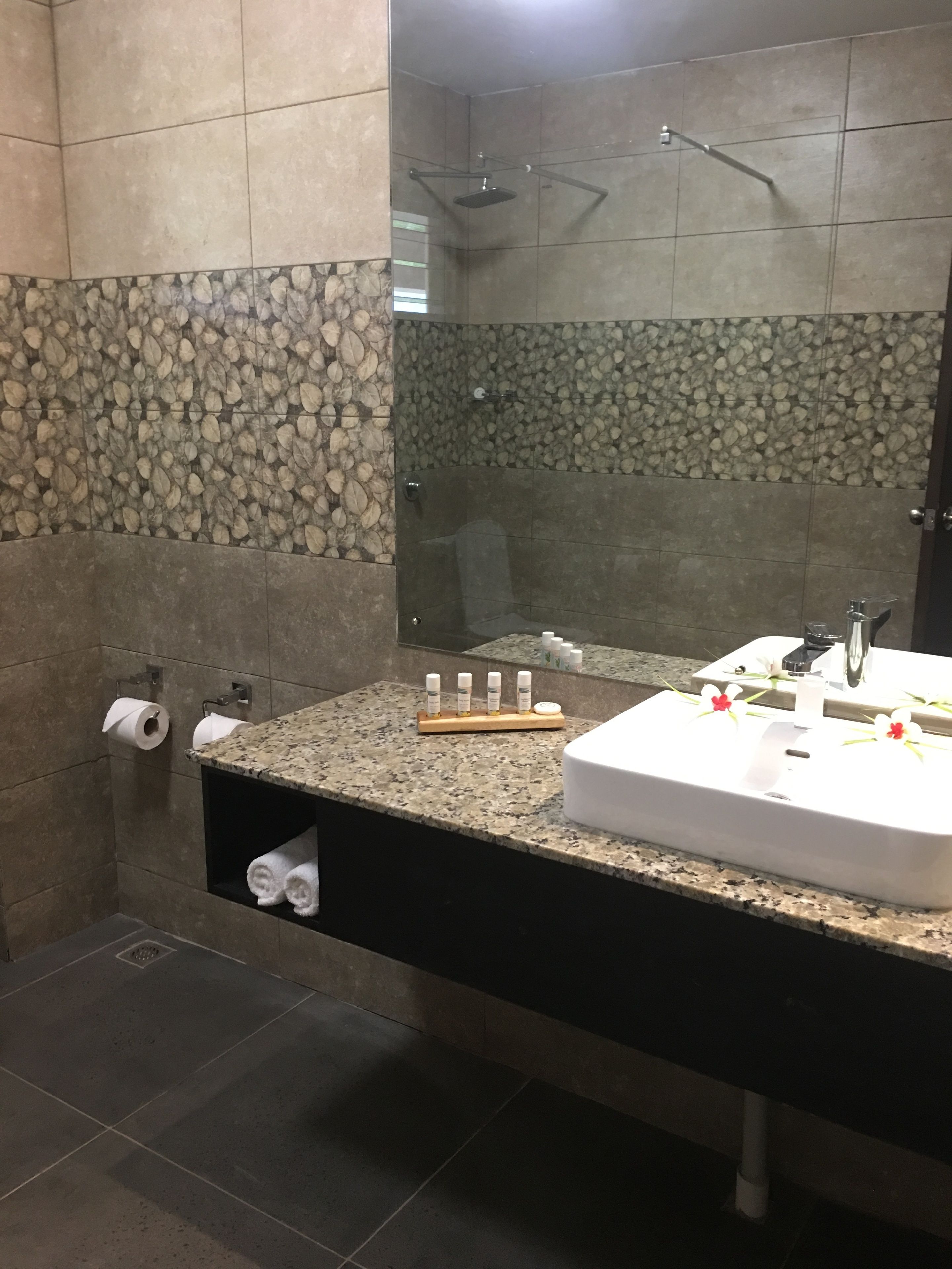 A bathroom with a granite countertop, a white sink, and a shower area with a stone wall.