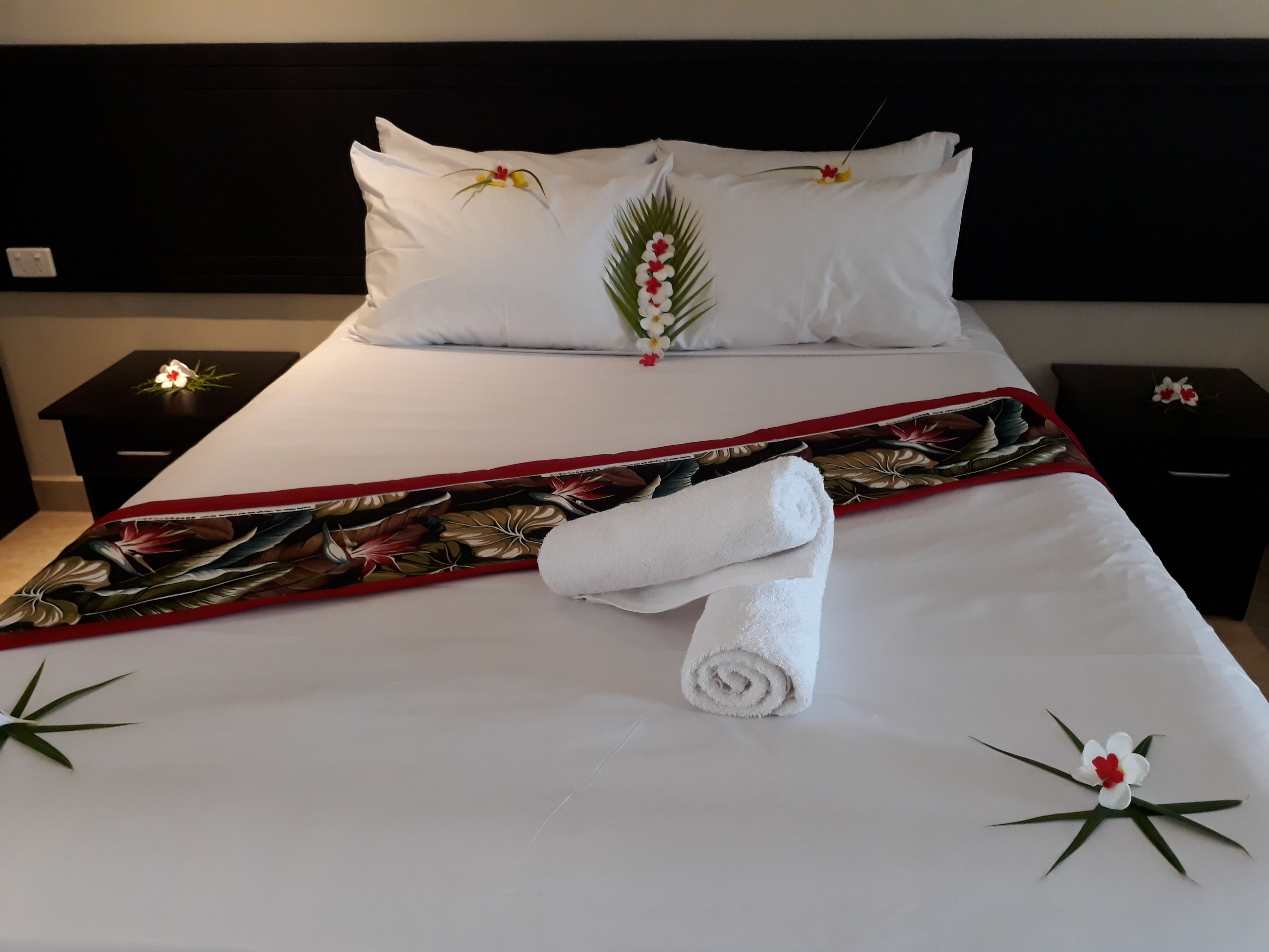 Un lit bien fait, avec du linge de lit blanc, une couvre-lit à motifs floraux et des coussins décoratifs ornés de fleurs.
