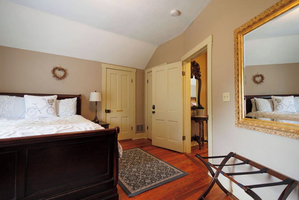 A bedroom with two beds, a wooden floor, a rug, and a mirror with a gold frame.