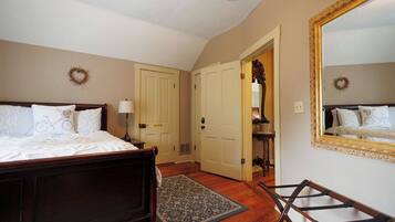 A bedroom with two beds, a wooden floor, a rug, and a mirror with a gold frame.