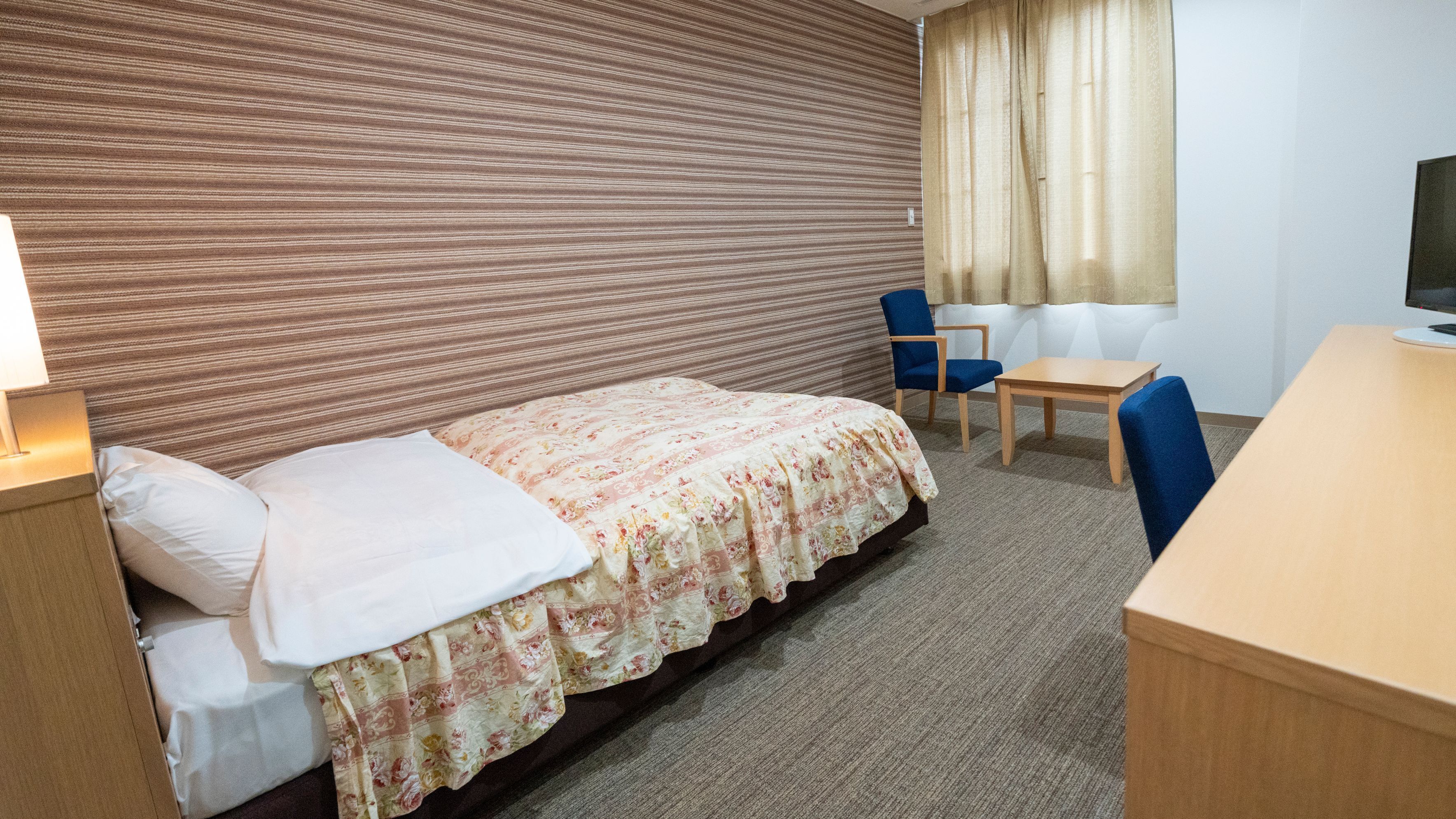 Ein Hotelzimmer mit Bett, Schreibtisch, Sessel, Fernseher und einem fensterbepflanzten Fenster.