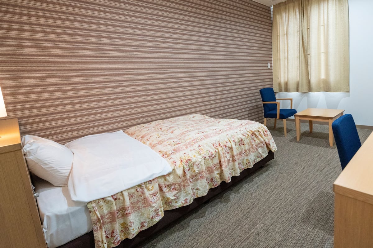 Une chambre d’hôtel équipée d’un lit, d’un bureau, d’une chaise, d’une télévision et d’une fenêtre avec des rideaux.