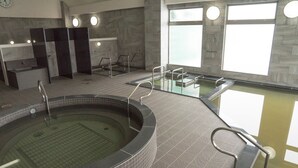 Uma área interna de piscina moderna, com várias piscinas, sauna e sala de trocas.