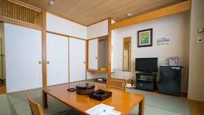 Quarto japonês tradicional com tatames, uma mesa baixa com um conjunto de chá, uma televisão e um frigorífico.