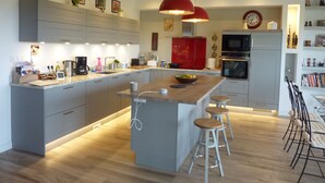 A modern kitchen with grey cabinets, a central island with stools, a red pendant light, and a clock on the wall.
