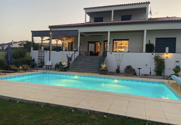 Una casa de dos pisos con piscina, un patio cubierto y una escalera que lleva al piso superior.