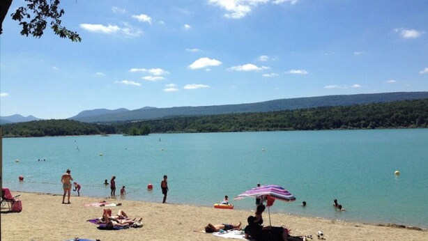 A beach with people sunbathing and swimming, a clear sky, and mountains in the background.