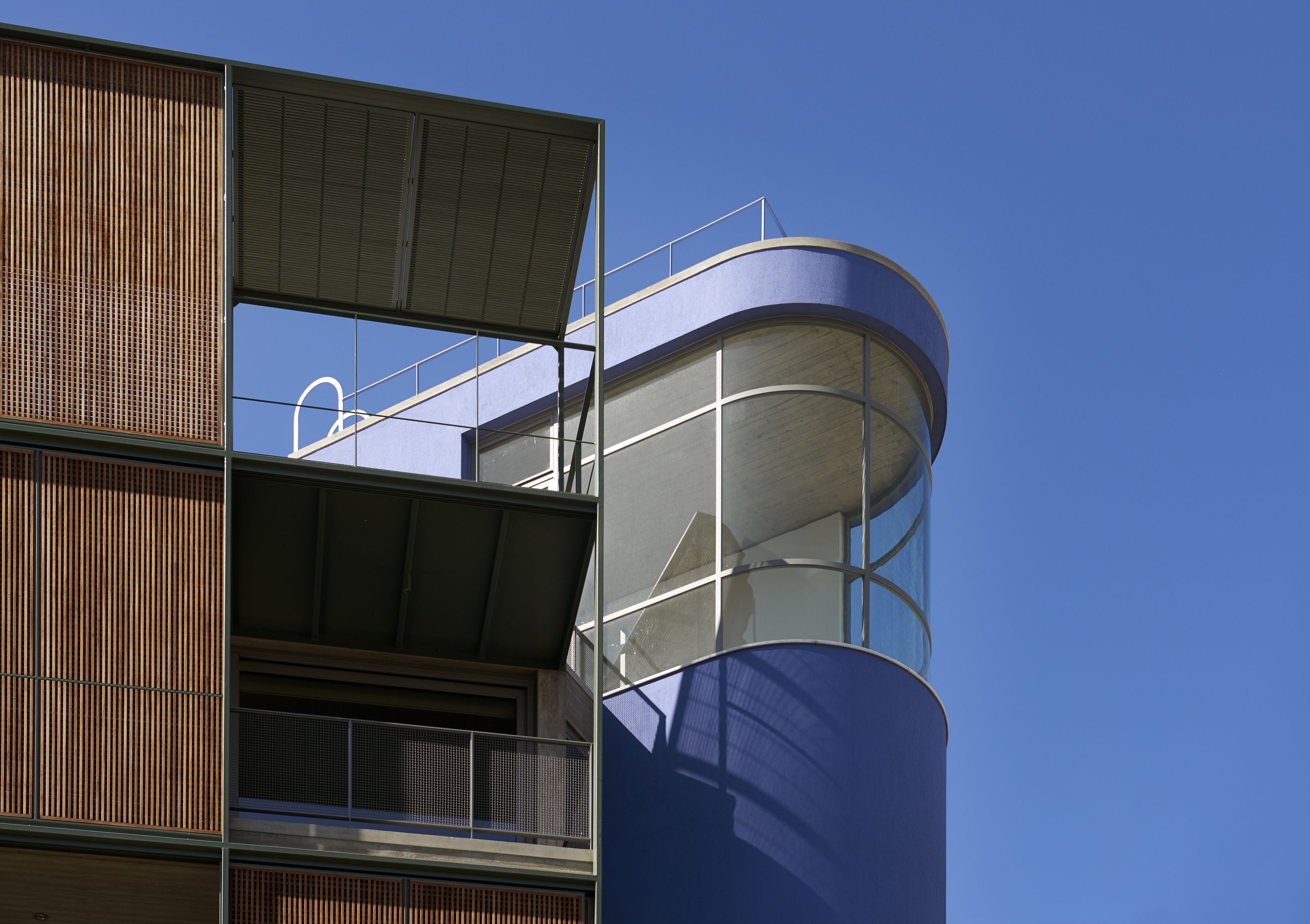 A modern building with a curved glass facade and a wooden slatted design on the left side.