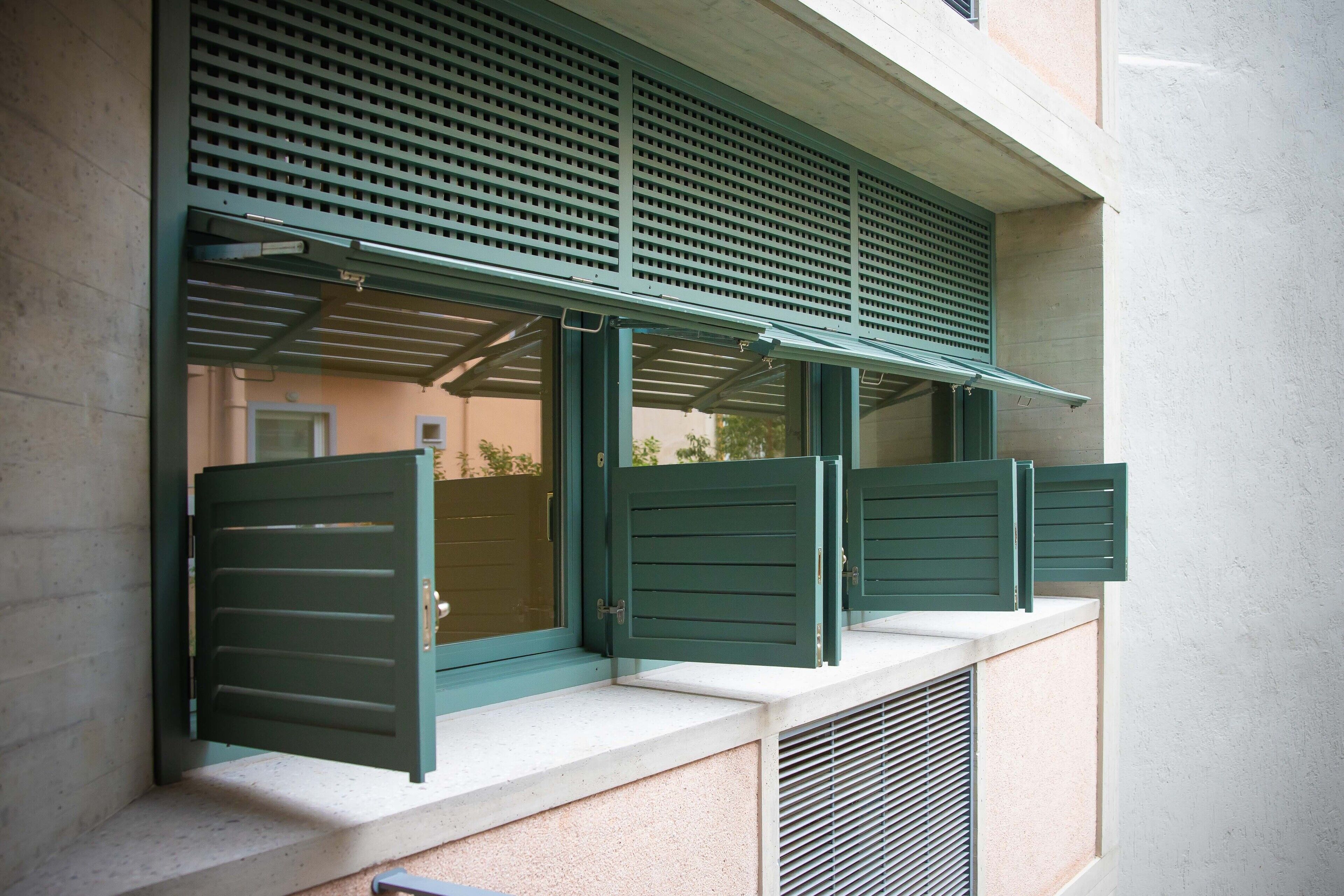 A window with green shutters and a metal grill.