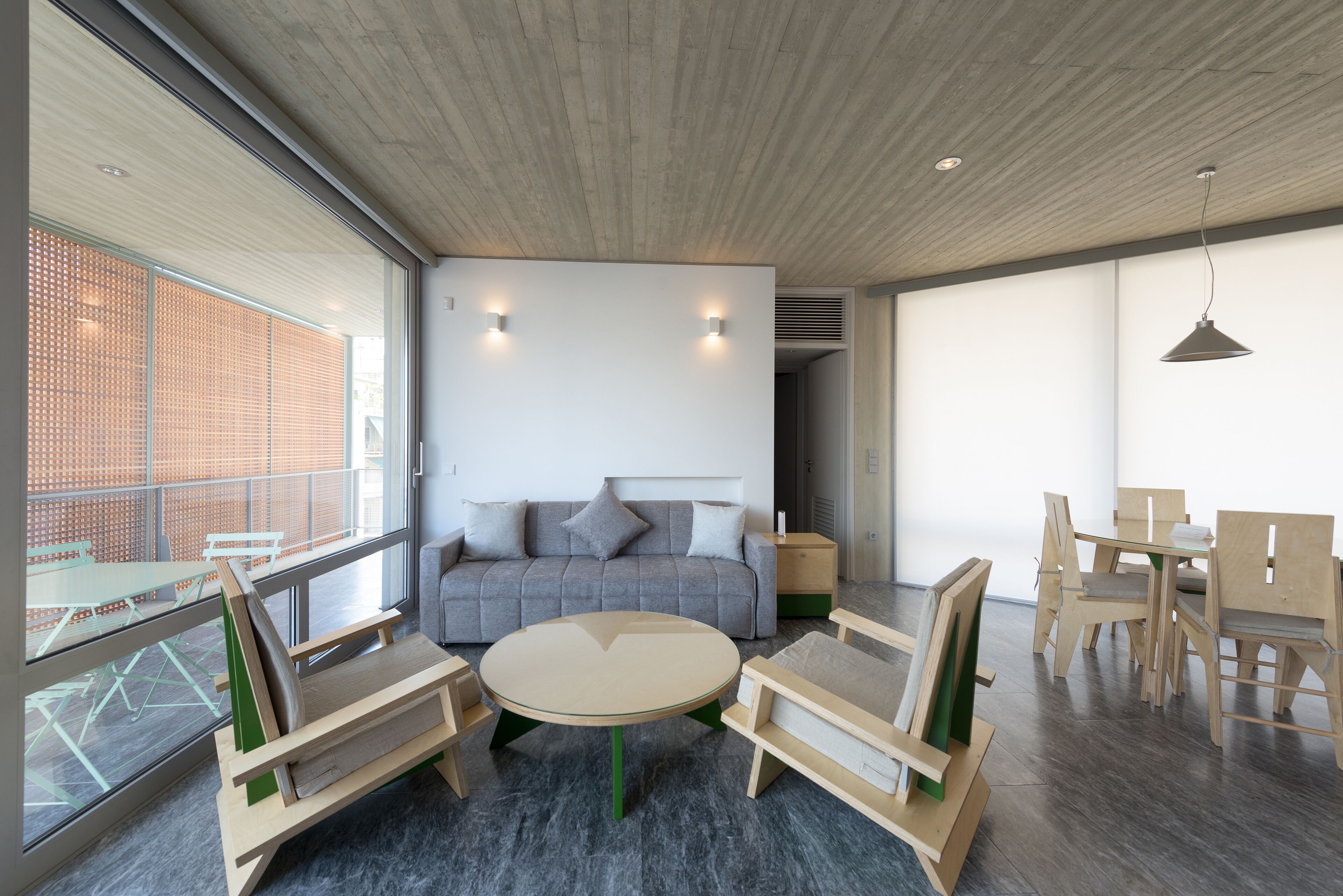 A modern living room with a sofa, coffee table, and wooden chairs. There is a large window with a view of a building outside.