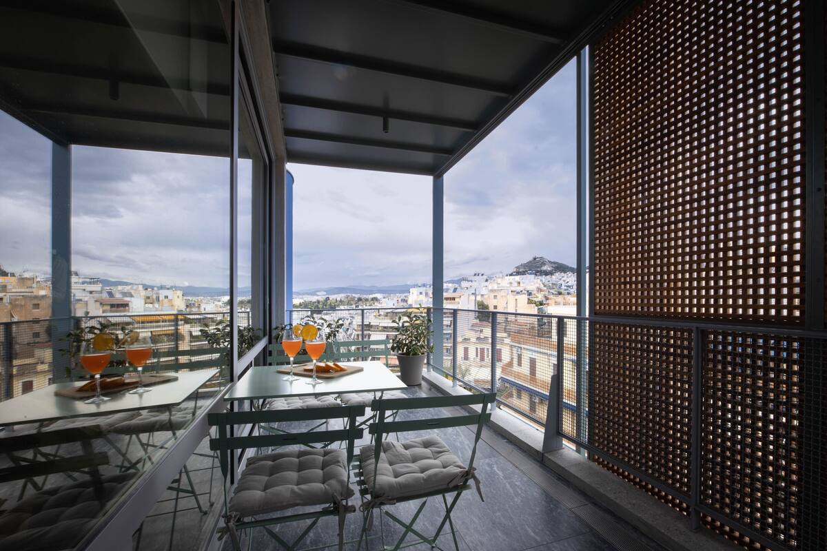 A balcony with a table set for two, a potted plant, and a view of the cityscape.