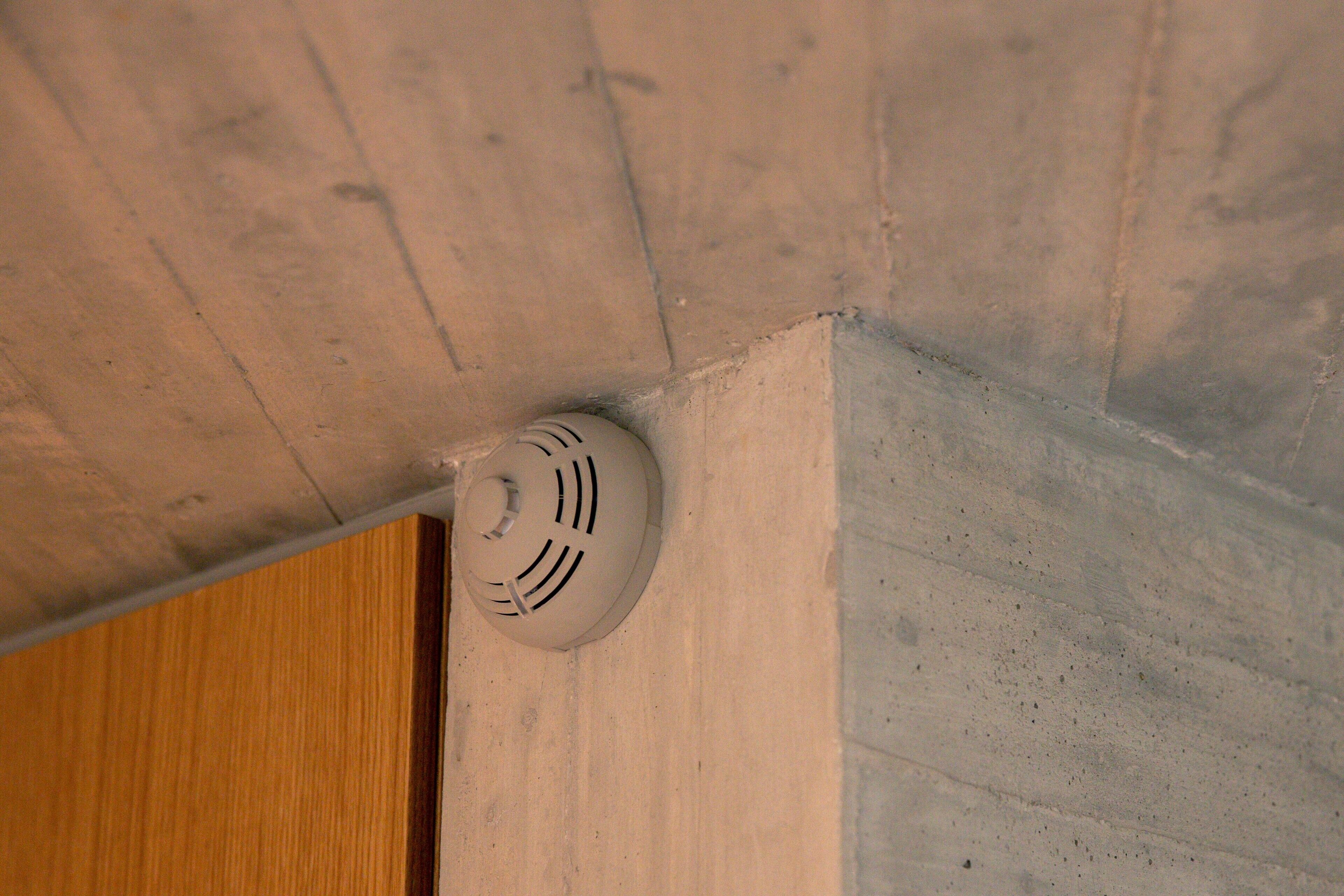 A ceiling vent in a room with a wooden door and a concrete wall.