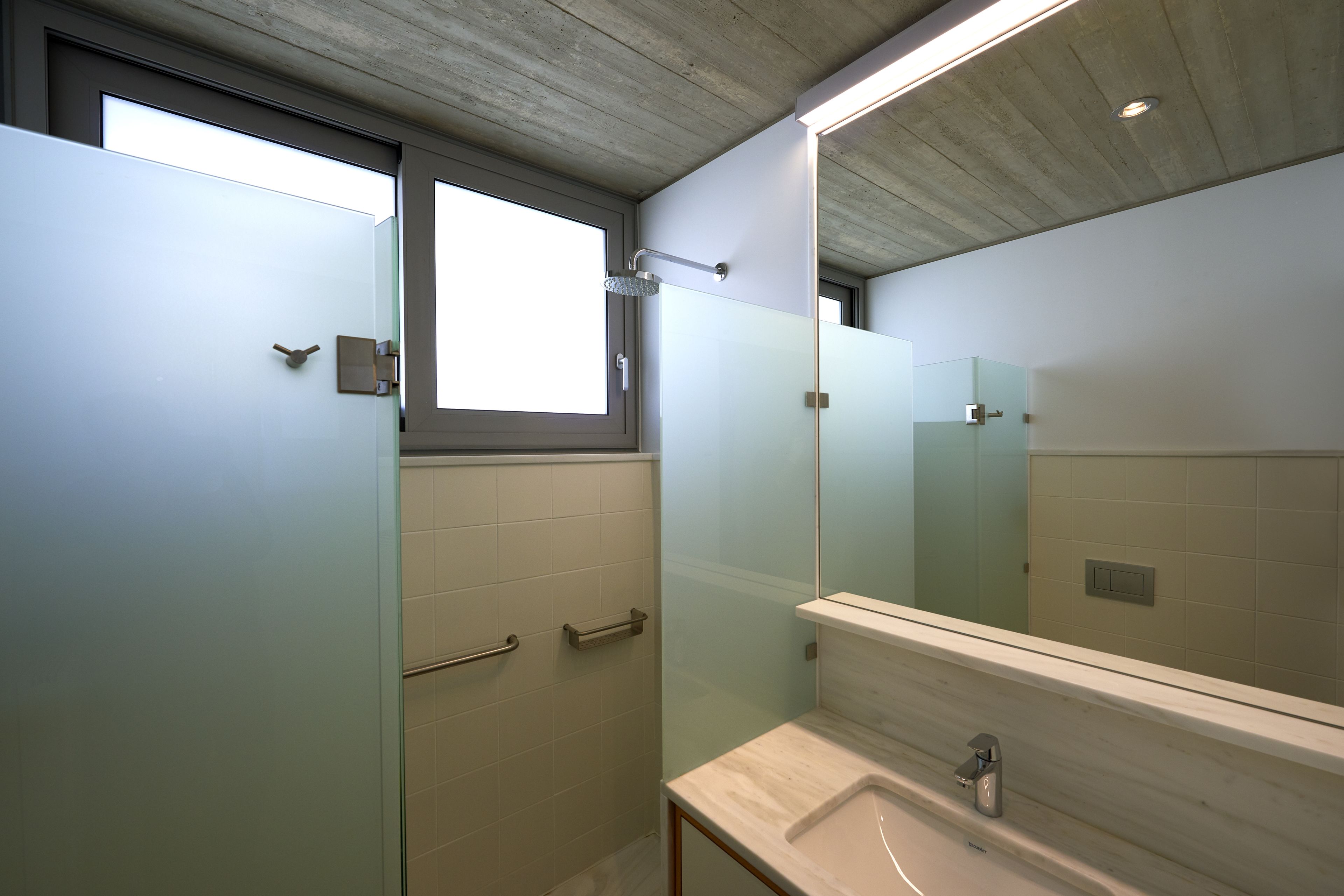 Un baño moderno con cabina de ducha de vidrio, un espejo grande y un lavabo blanco.