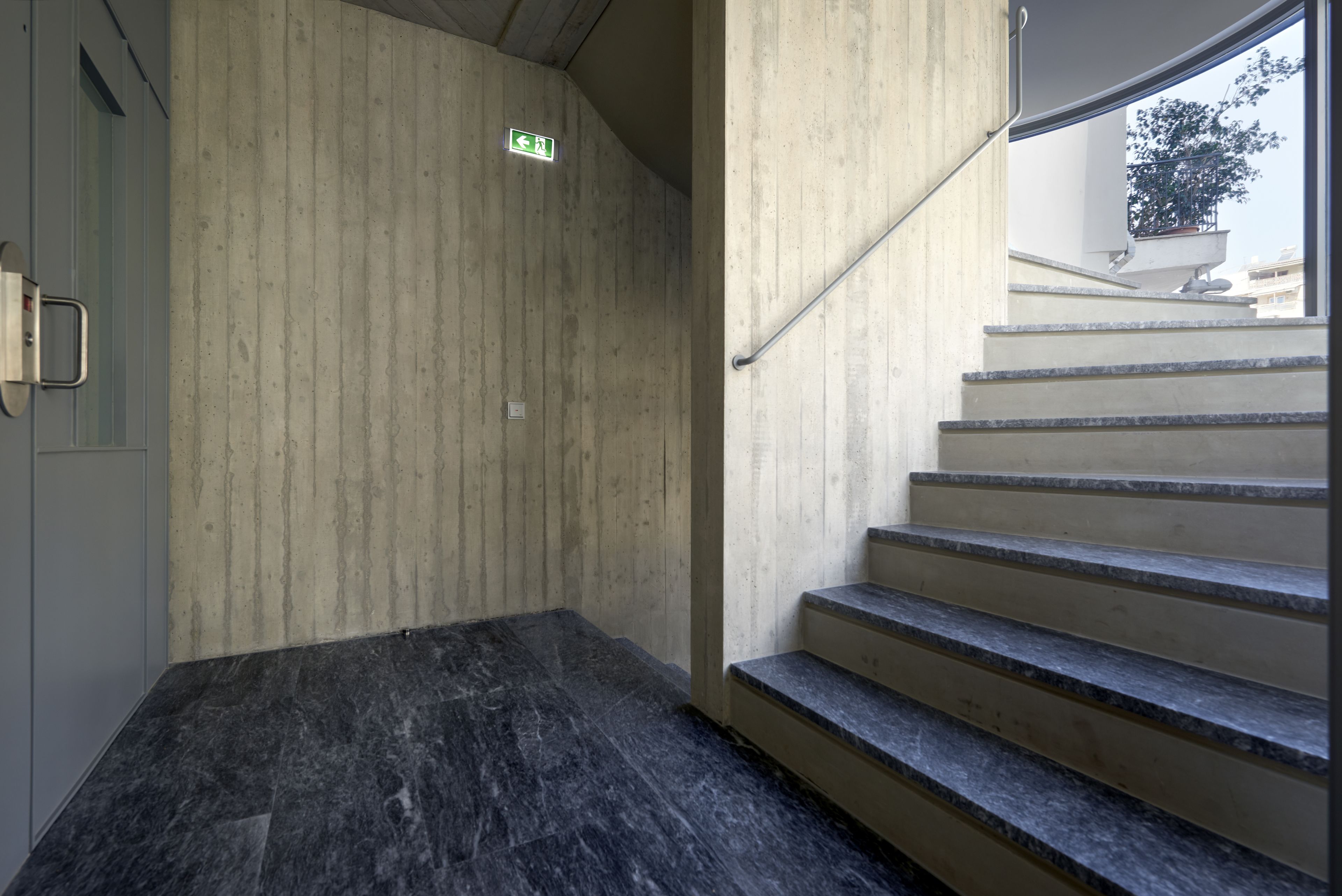A staircase with a handrail, a green exit sign, and a concrete wall.