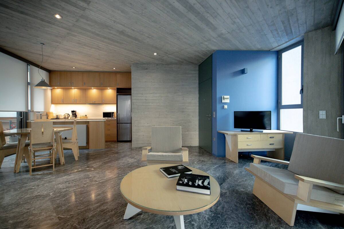 A modern living room with a glass coffee table, two armchairs, a sofa, and a television.