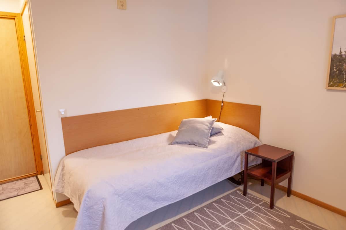 Un lit simple avec une tête de lit en bois, une table de chevet, une lampe et un tapis.