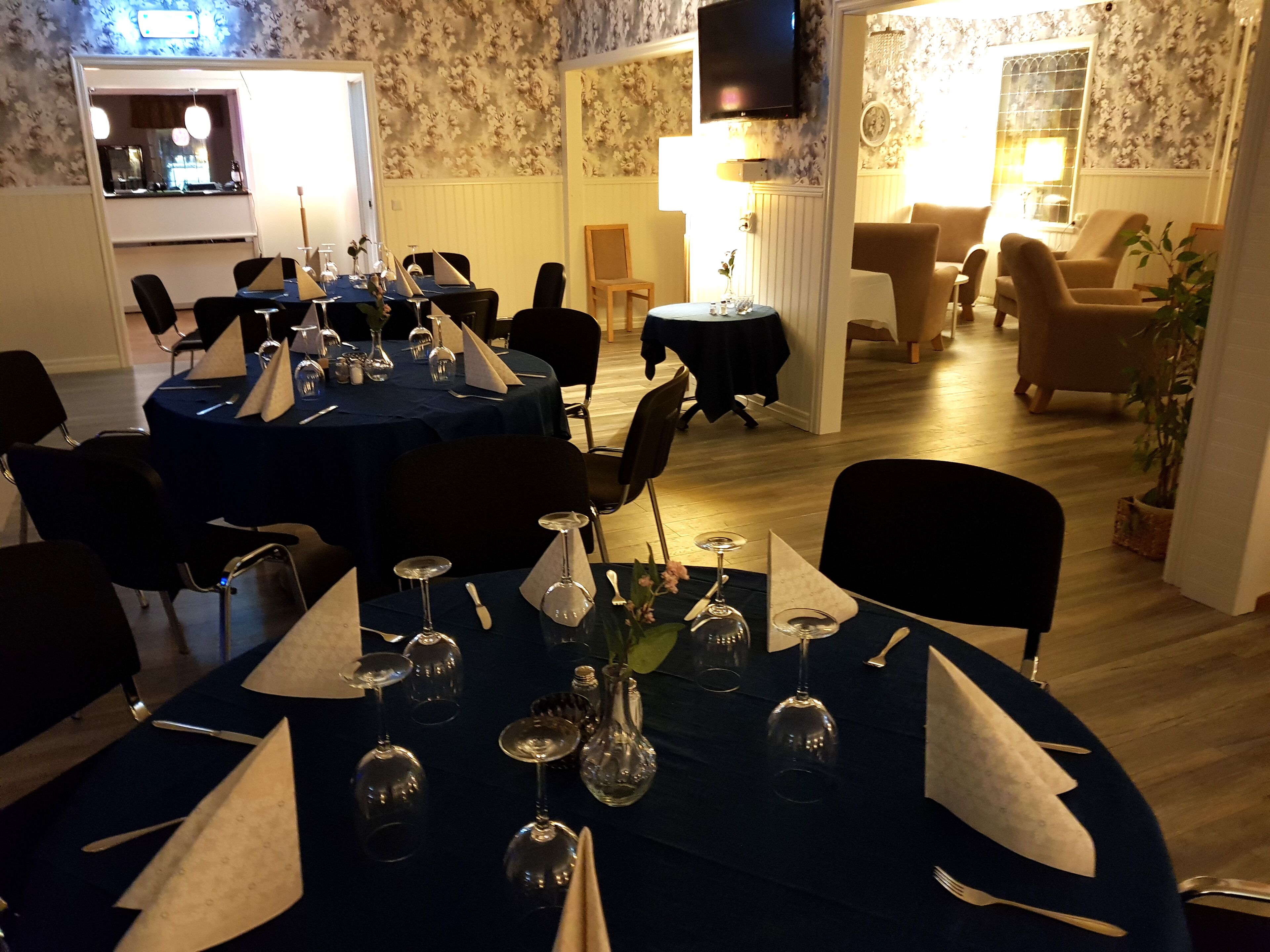 A dining area with round tables set for a meal, featuring wine glasses and cutlery.