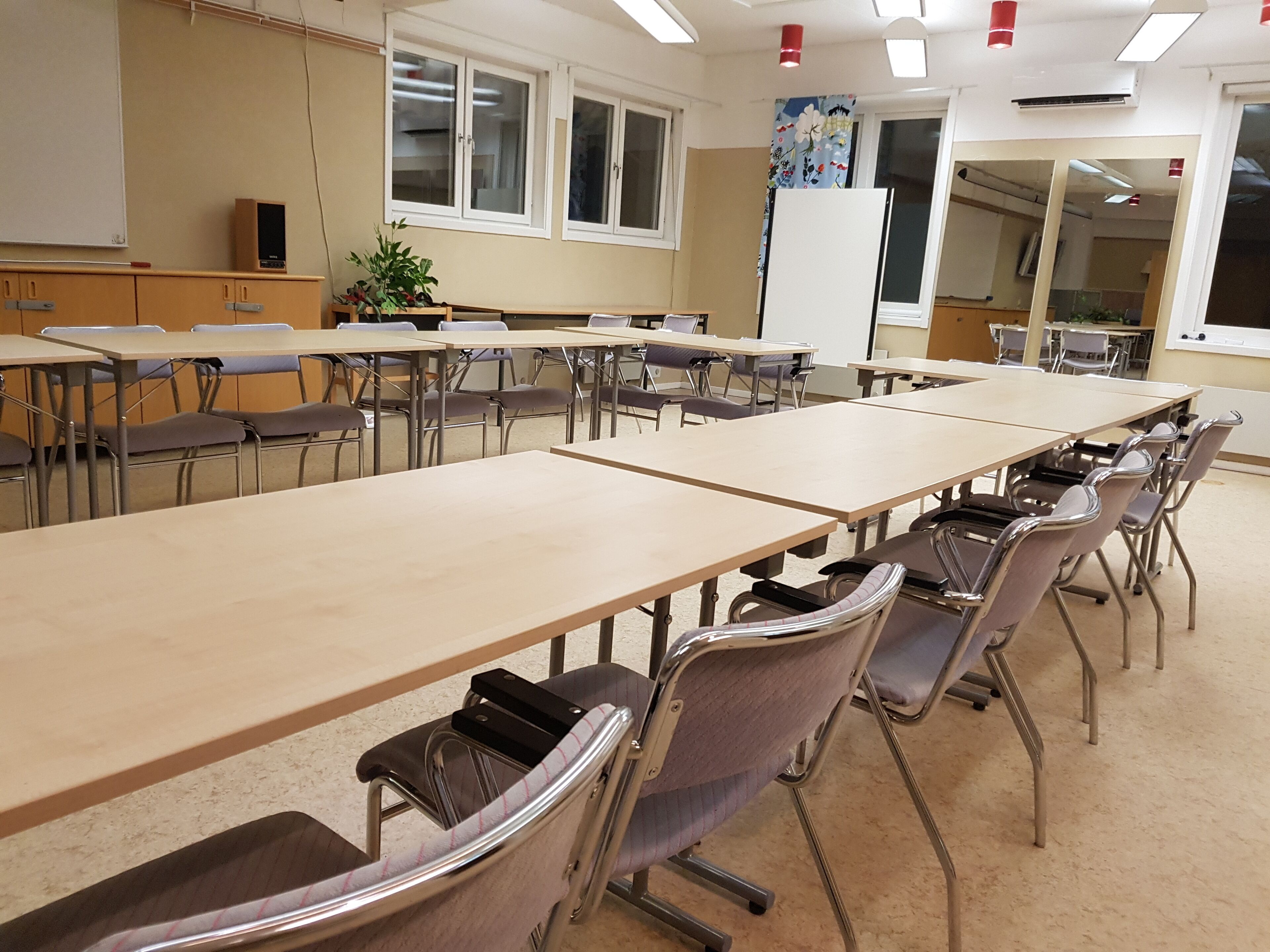 A classroom with long tables and chairs, a whiteboard, and windows with curtains.
