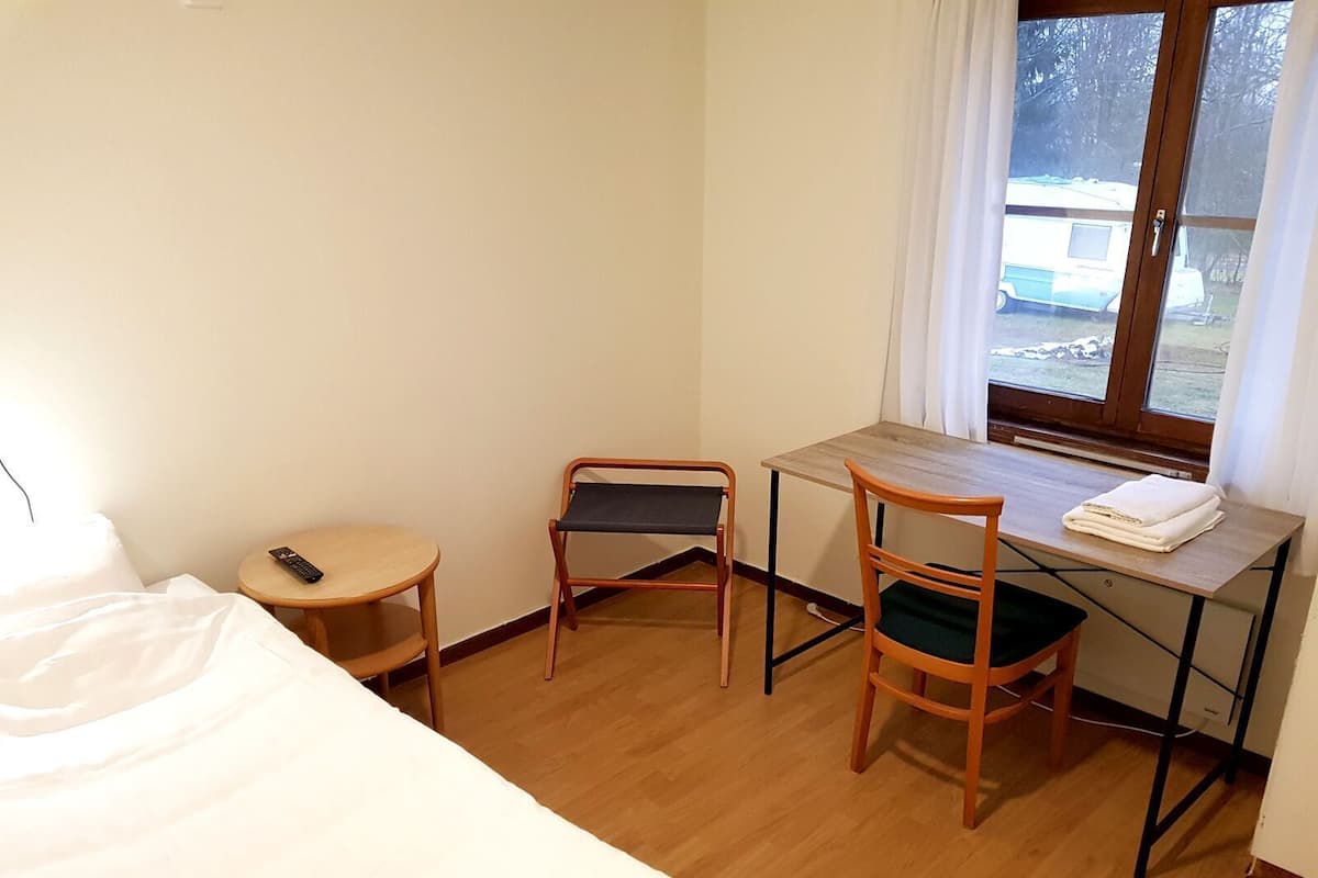 Une petite chambre d’hôtel comprenant un lit, un bureau, une chaise, une télécommande et une fenêtre donnant sur un véhicule à l’extérieur.