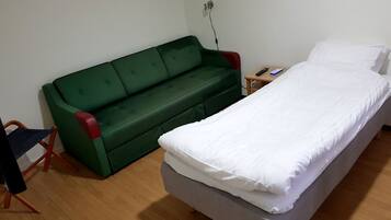 A small, simple room with a single bed, a green sofa, and a small table with a remote control.