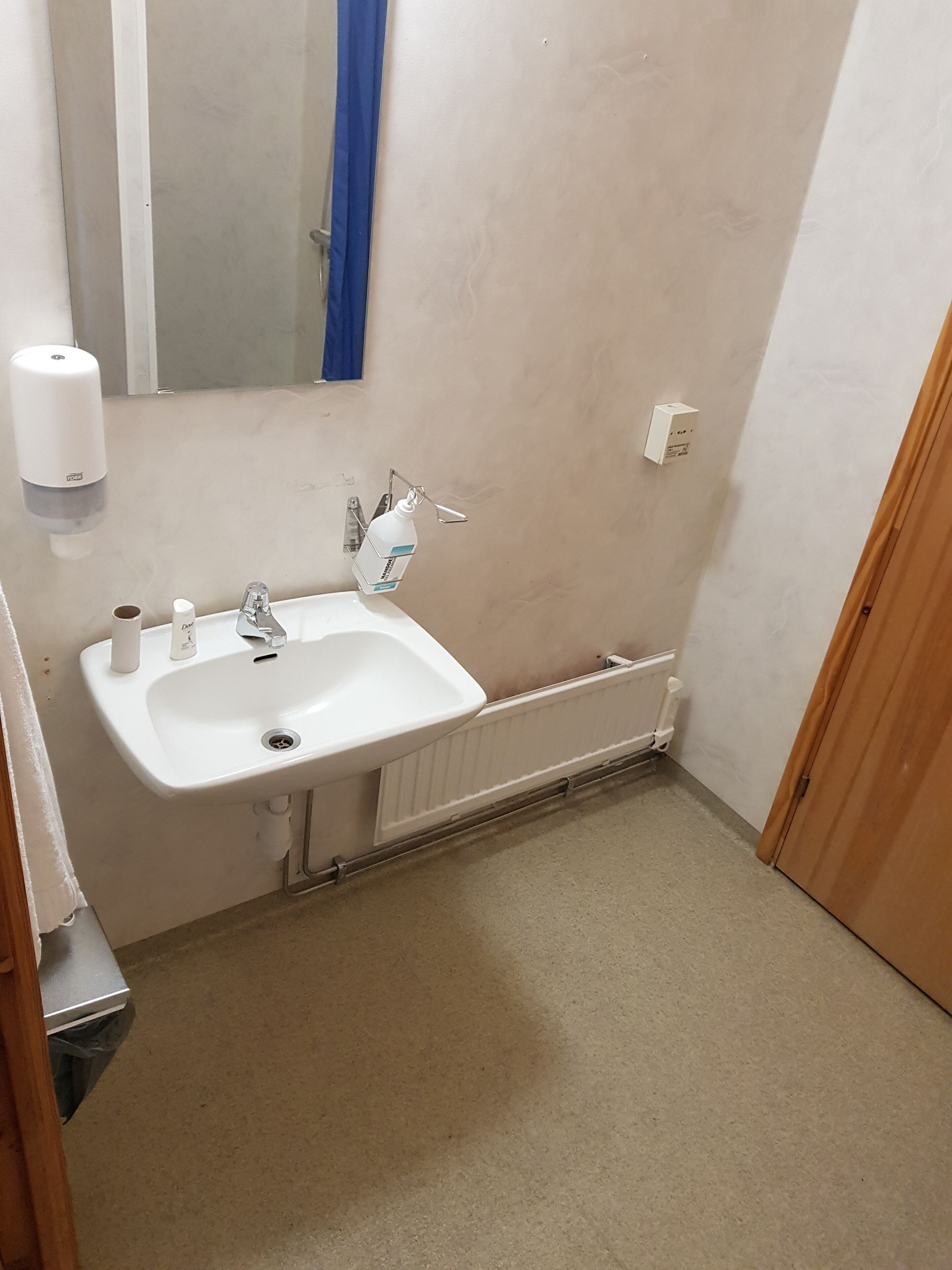A small bathroom with a white sink, a mirror, a blue shower curtain, and a white radiator.
