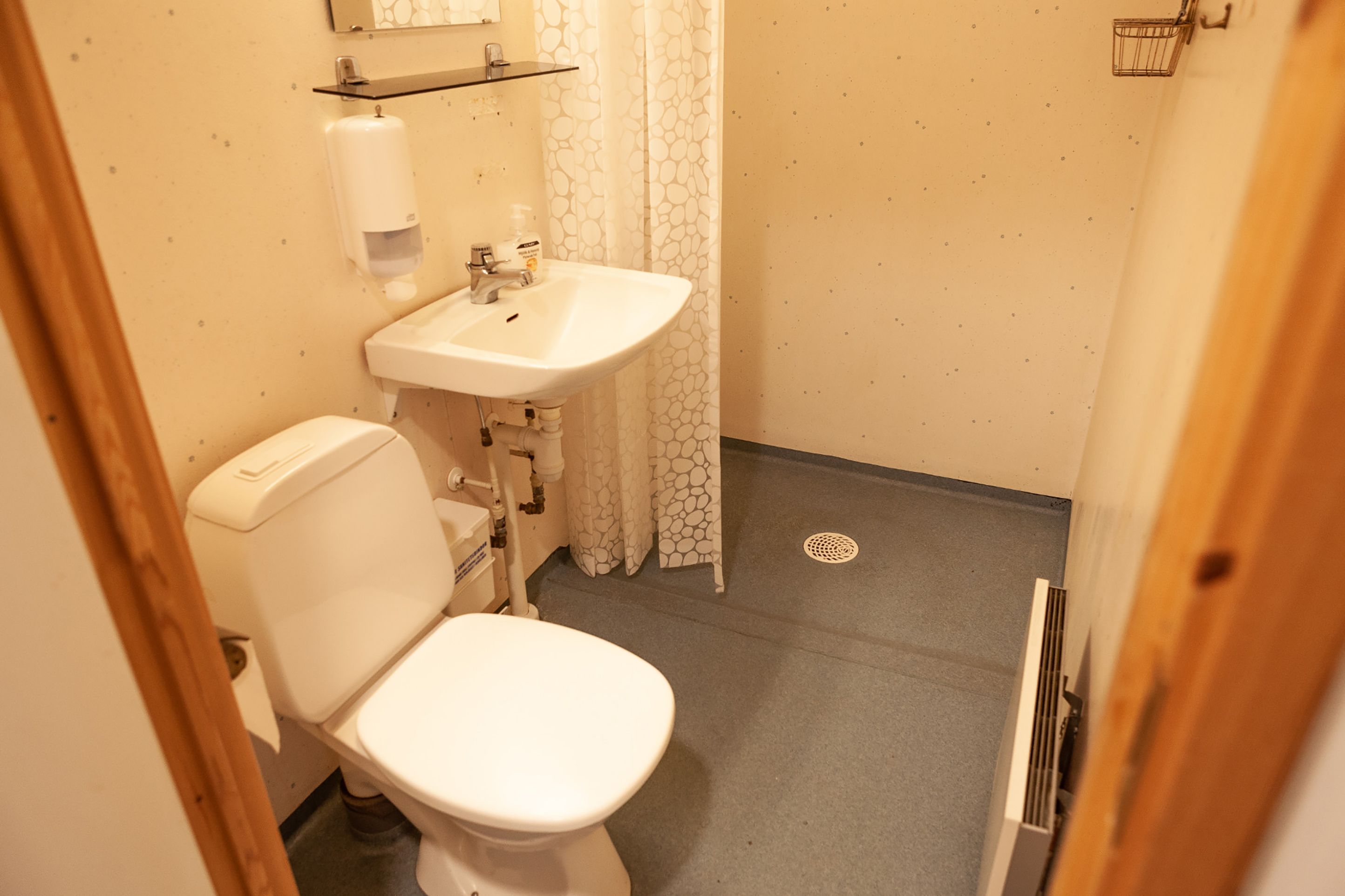 Pieni kylpyhuone, jossa on wc, pesuallas ja suihkuverho.
