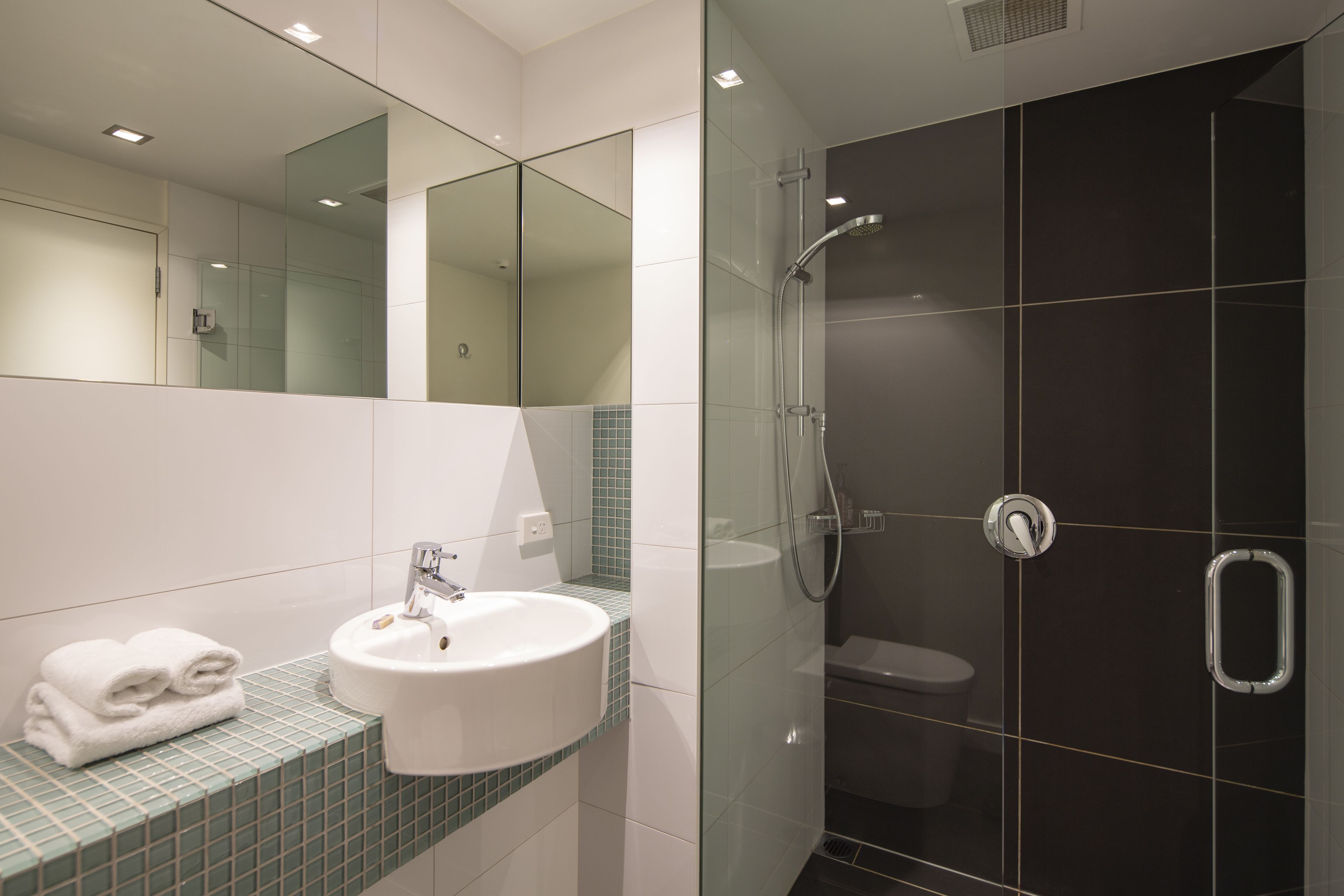 Une salle de bain moderne avec une douche à parois de verre, un lavabo blanc et un miroir.