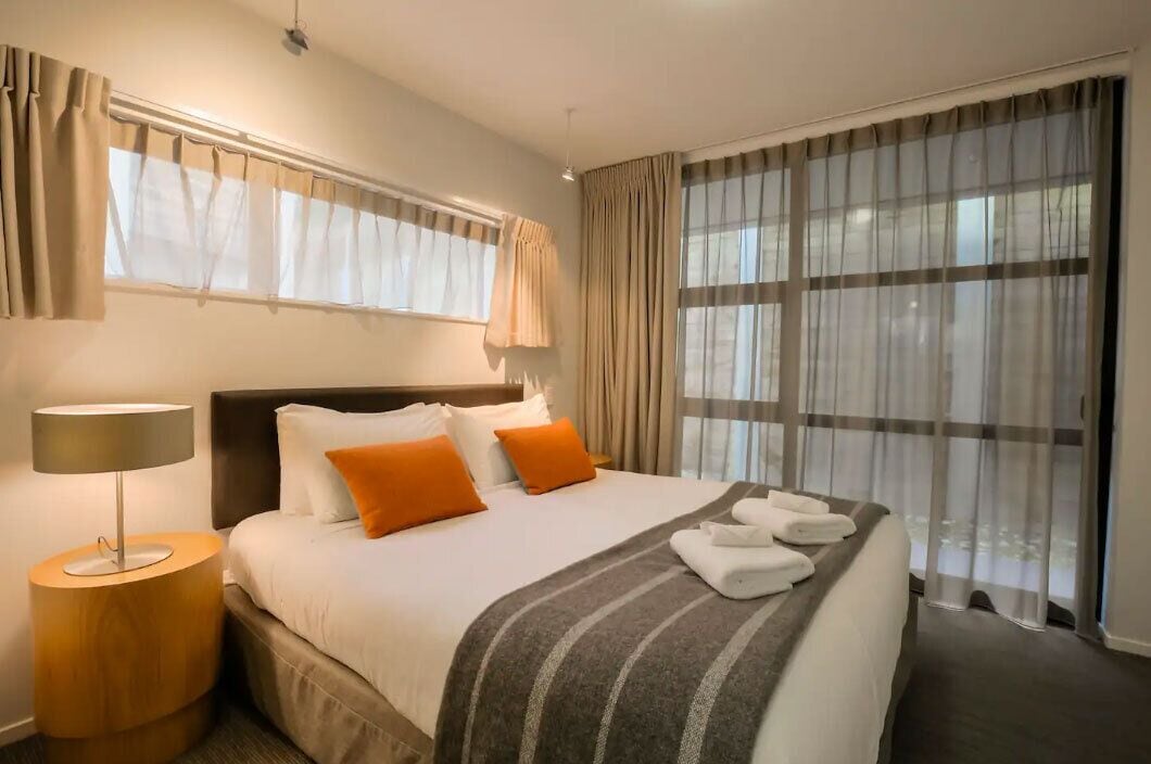 Une chambre d’hôtel avec un lit, une lampe de chevet, une fenêtre avec des rideaux et une vue sur l’extérieur.