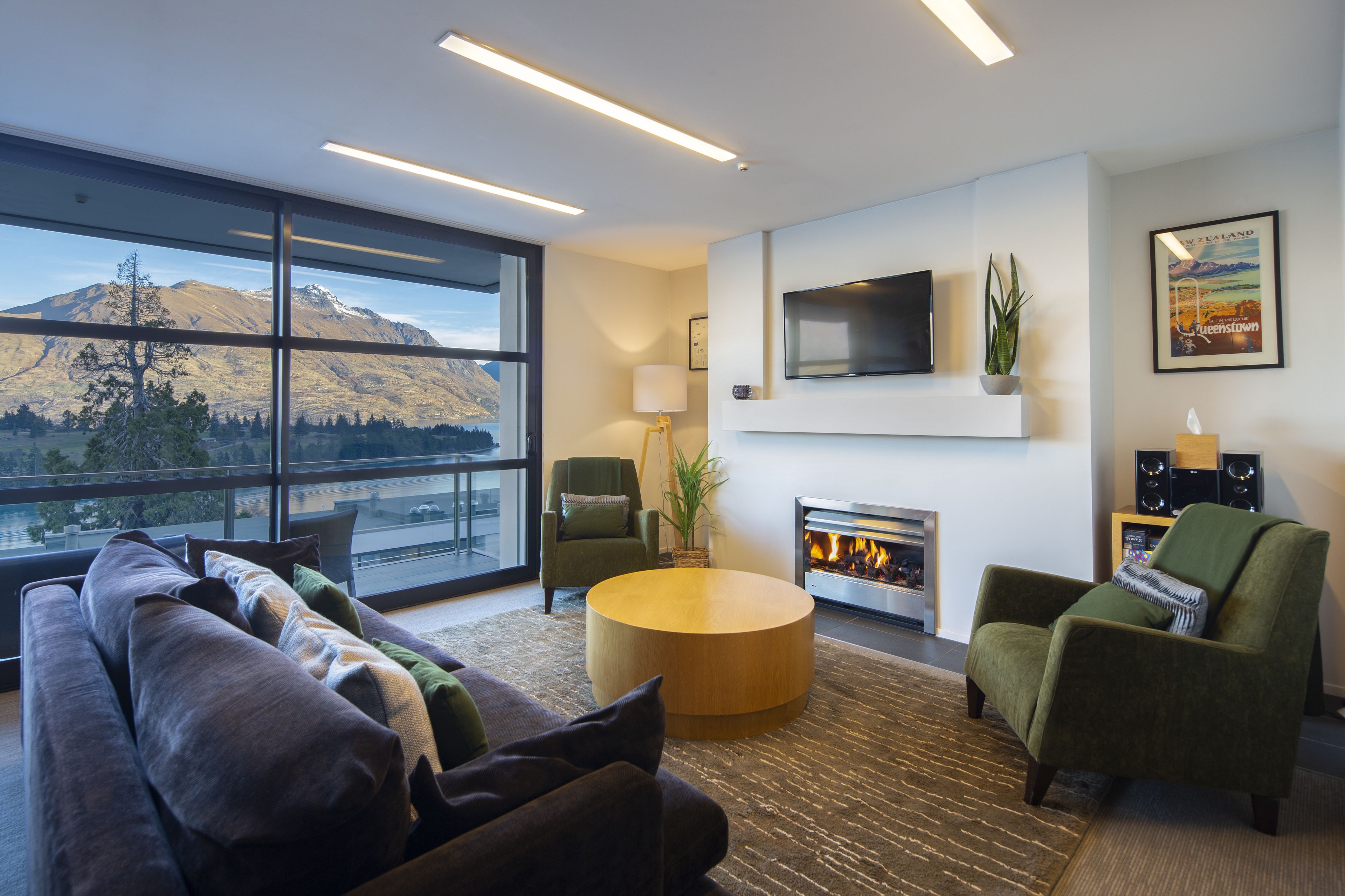 A modern living room with a large window, a fireplace, a flat-screen TV, and a cozy seating area.