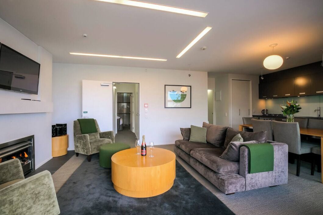 Een moderne woonkamer met een open haard, een ronde salontafel, een bank en een aan de muur bevestigde televisie.