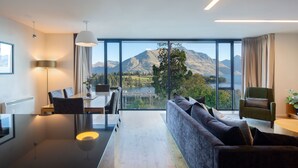 A modern living room with a large window offering a mountain view, a dining area, and a cozy seating area. - Panorama Terrace Apartments, Element Escapes (Queenstown)