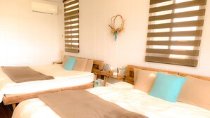 A hotel room with two beds, each with a brown blanket, a wooden headboard, and a small bedside table with a lamp and a phone. - Resort Villa Kouri island Aqua Blue (Nakijin)