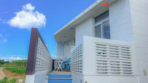 A modern building with a white exterior, a set of stairs leading to a door, and a small outdoor seating area with a table and chairs. - Resort Villa Kouri island Aqua Blue (Nakijin)