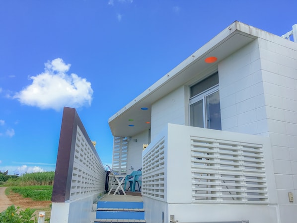 Um edifício moderno com fachada branca, um conjunto de degraus que levam a uma porta e uma pequena área externa com mesa e cadeiras.