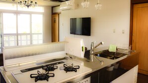 A modern kitchen with a gas stove, stainless steel sink, and a flat-screen TV mounted above the counter. - Resort Villa Kouri island Aqua Blue (Nakijin)