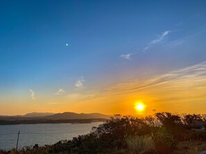 Um pôr do sol sobre a água, com montanhas ao fundo.