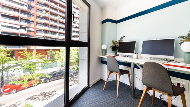 A modern office space with two desks, chairs, and large windows offering a view of a residential area. - Moontels Valencia Alameda 41 (Valencia)