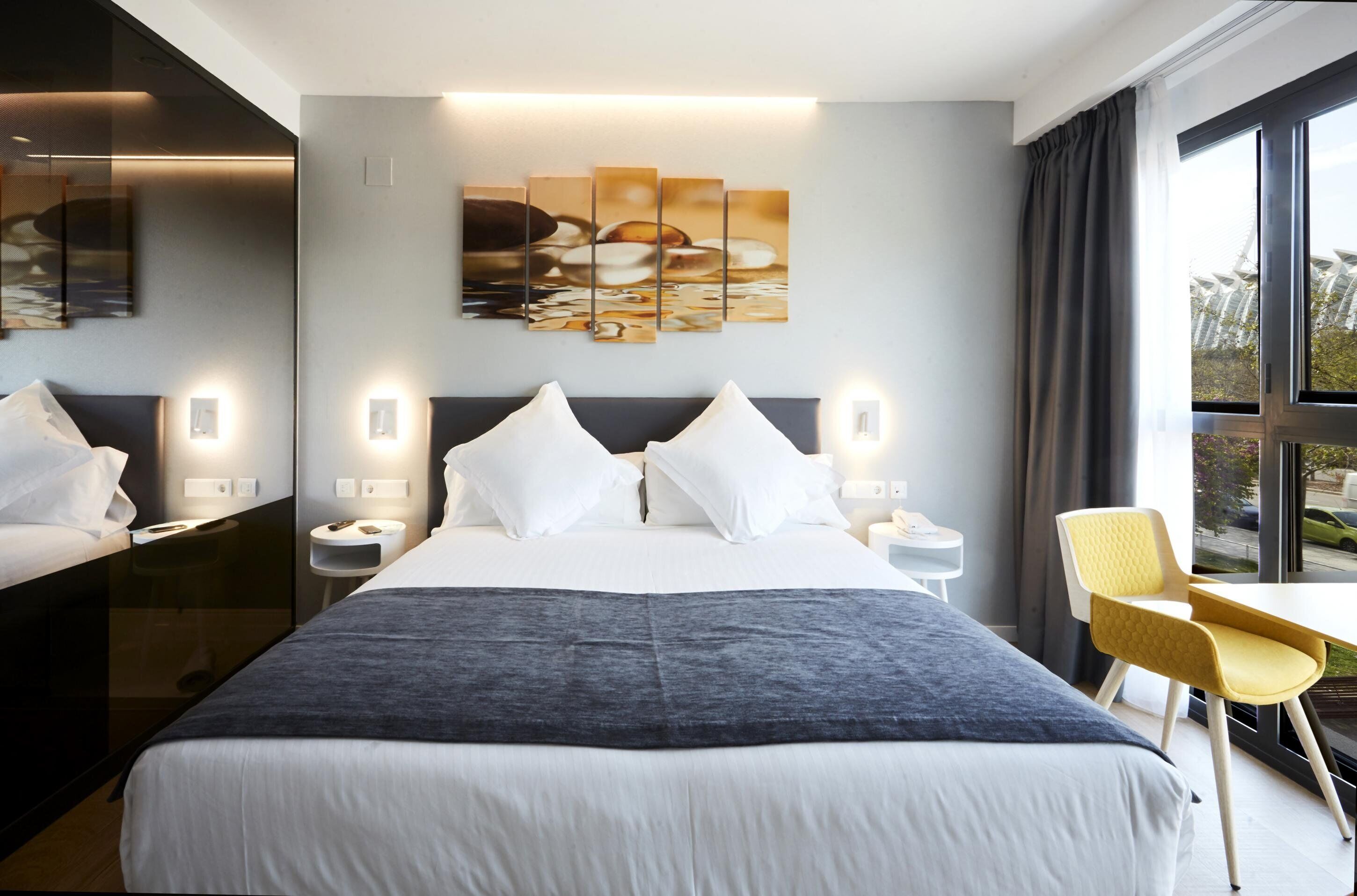 A hotel room with a large bed, a desk, a chair, and a view of the outside.