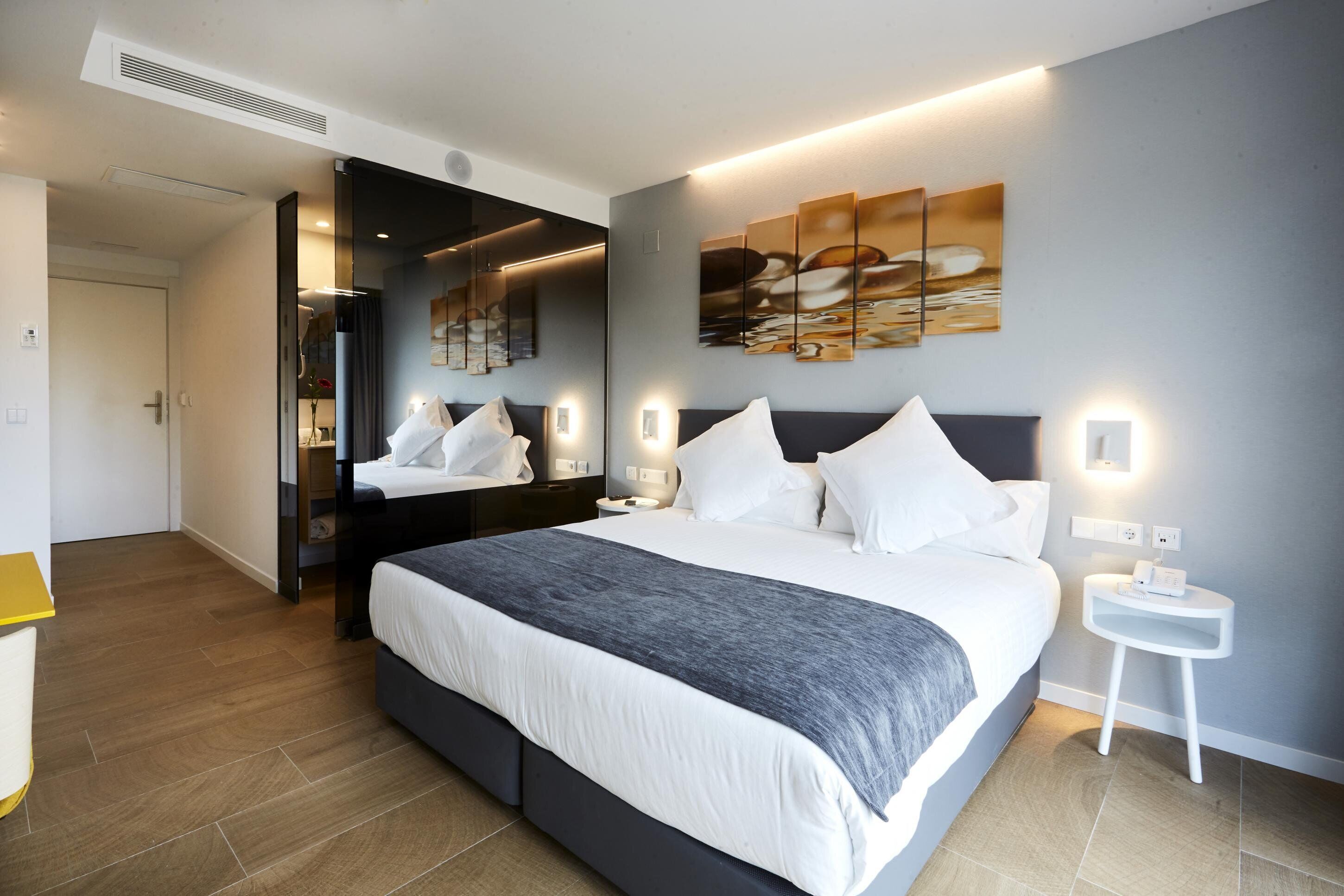 Una habitación de hotel moderna con una cama grande, mesitas de noche, un espejo y cuadros en la pared.
