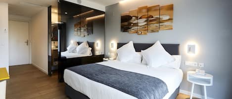 Una habitación de hotel moderna con una cama grande, mesitas de noche, un espejo y cuadros en la pared.